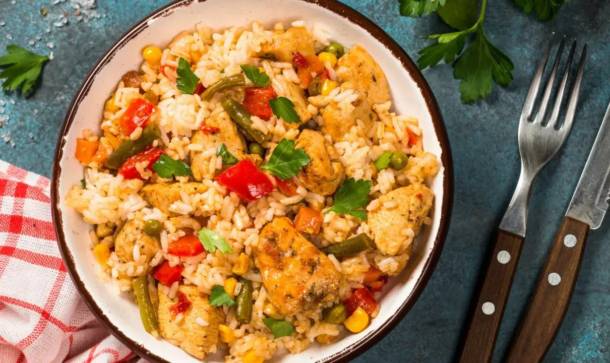 Pyszne risotto z kurczakiem i warzywami, podane w misce, obok widelca i noża.