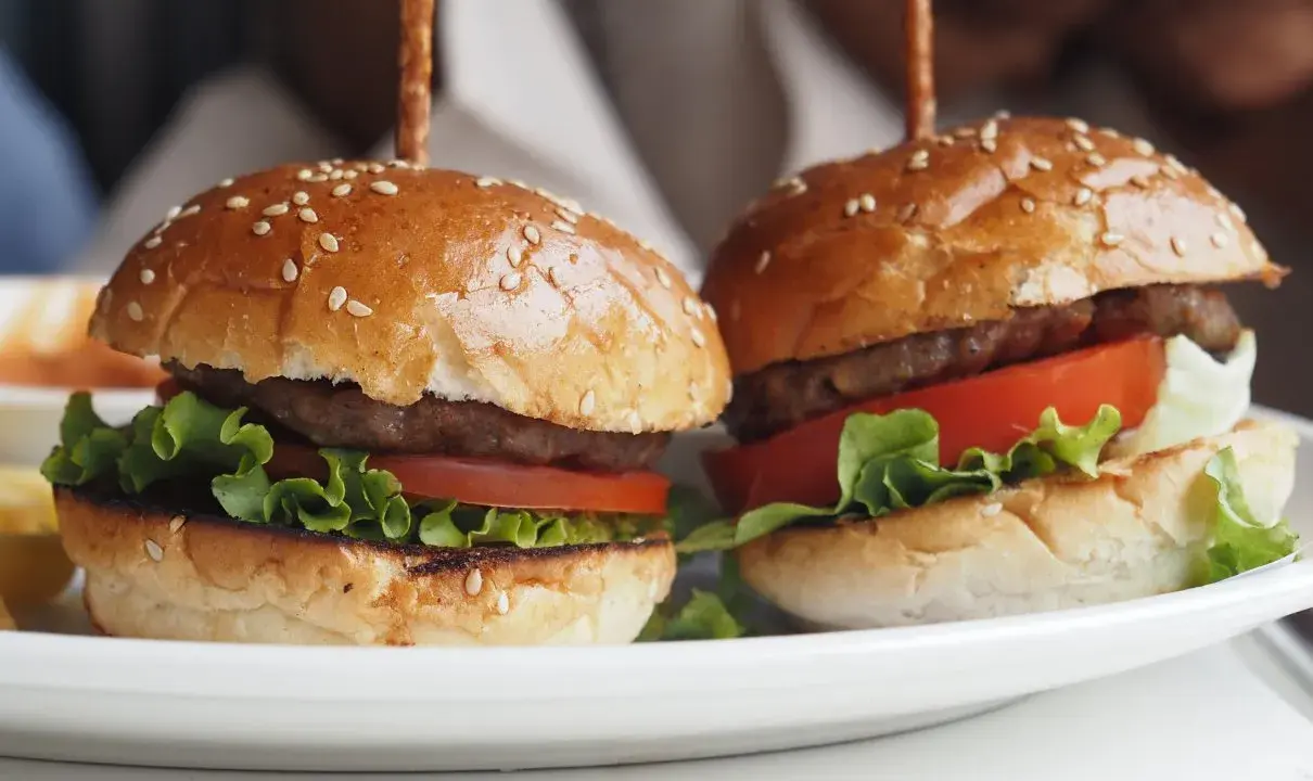 Dwa apetyczne mini burgery z sezamem, sałatą i pomidorem. Idealne na imprezę, oto prosty mini burgery przepis.