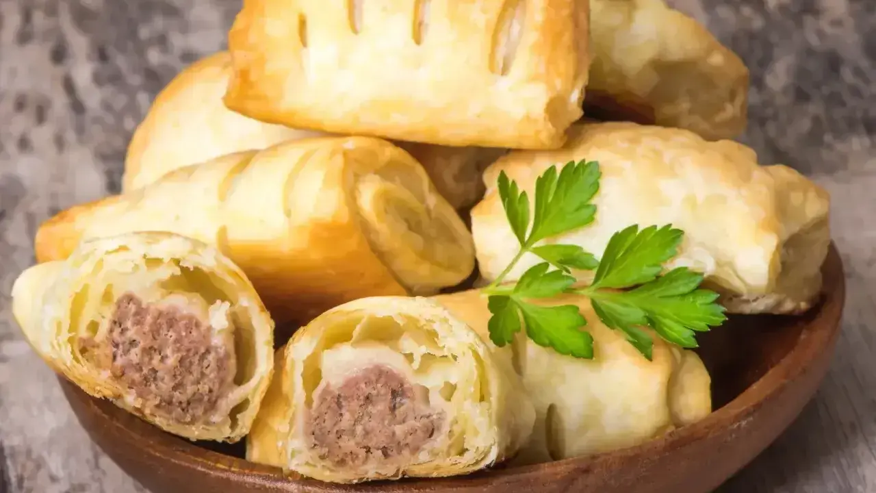 Stos pieczonego ciasta francuskiego z kiełbaską w środku, ozdobione natką pietruszki.