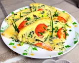 Pyszny omlet ze szpinakiem, pomidorami i szczypiorkiem, pokrojony w trójkąty, podany na talerzu z kwiatowym wzorem.