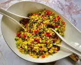 Kolorowa sałatka z kaszą bulgur, pomidorami, ogórkiem i papryką, podana w białej misie z dwoma białymi łopatkami.