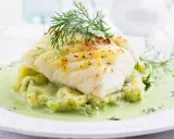 Pyszna ryba w sosie koperkowym, podana na purée ziemniaczanym z dodatkiem świeżego koperku. Danie wygląda apetycznie i aromatycznie.