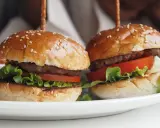 Dwa apetyczne mini burgery z sezamem, sałatą i pomidorem. Idealne na imprezę, oto prosty mini burgery przepis.