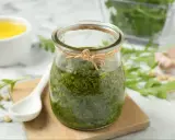 Słoik domowego pesto z rukoli, obok biała łyżeczka, piniowe orzeszki i czosnek. Idealne do makaronu!