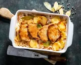 Pieczony schab w kapuście kiszonej z ziemniakami, podany w białym naczyniu, ozdobiony liśćmi laurowymi.