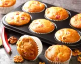 Pyszne muffinki z rabarbarem, świeże i pachnące, gotowe do podania. Obok leżą łodygi rabarbaru i orzechy włoskie.