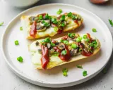 Dwie zapiekanki z pieczarkami, serem i keczupem, posypane szczypiorkiem, na talerzu.