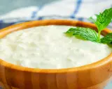 Domowy sposób na to, jak zrobić zsiadłe mleko. Gęsty, biały produkt w drewnianej misce, ozdobiony świeżą miętą.