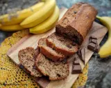 Pyszny chlebek bananowy z czekoladą, pokrojony w plastry, obok świeżych bananów i kostek czekolady.