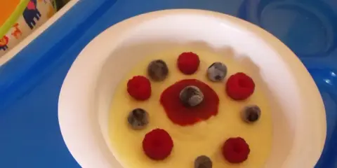 Pyszna kasza manna na wodzie, udekorowana malinami i borówkami, wygląda jak słoneczko na talerzu.