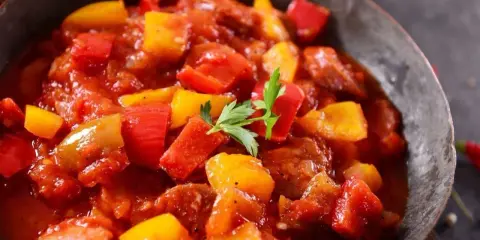 Pyszne leczo z pieczarkami, papryką i kiełbasą w sosie pomidorowym, udekorowane natką pietruszki.