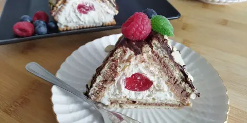 Trójkątny deser z kremem i wiśnią, przypominający chatkę Baby Jagi, udekorowany malinami i migdałami.