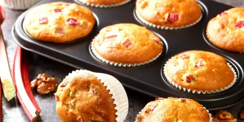 Pyszne muffinki z rabarbarem, świeże i pachnące, gotowe do podania. Obok leżą łodygi rabarbaru i orzechy włoskie.