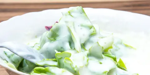 Chrupiąca sałata ze śmietaną, podana w białej misce, z widelcem gotowym do nabrania porcji.