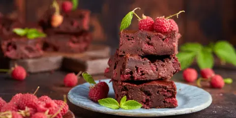 Stos puszystych brownie z malinami, ozdobiony świeżymi malinami i listkami mięty.