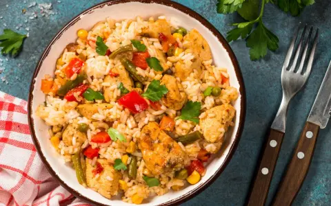 Pyszne risotto z kurczakiem i warzywami, podane w misce, obok widelca i noża.