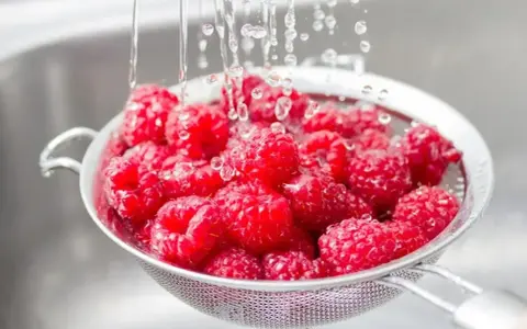 Woda spływa po świeżych malinach w durszlaku. Czy maliny się myje? Tak, aby były gotowe do jedzenia!
