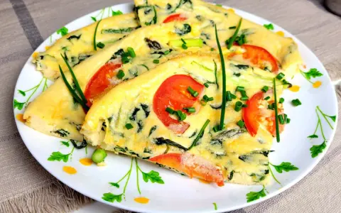 Pyszny omlet ze szpinakiem, pomidorami i szczypiorkiem, pokrojony w trójkąty, podany na talerzu z kwiatowym wzorem.