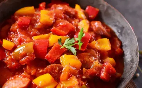 Pyszne leczo z pieczarkami, papryką i kiełbasą w sosie pomidorowym, udekorowane natką pietruszki.