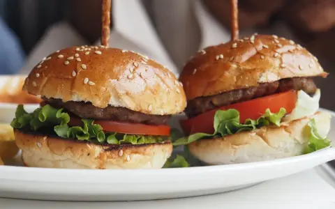 Dwa apetyczne mini burgery z sezamem, sałatą i pomidorem. Idealne na imprezę, oto prosty mini burgery przepis.