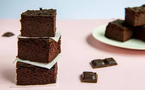 Ciemne, wilgotne brownie z fasoli ułożone w wieżę, obok kawałki czekolady.