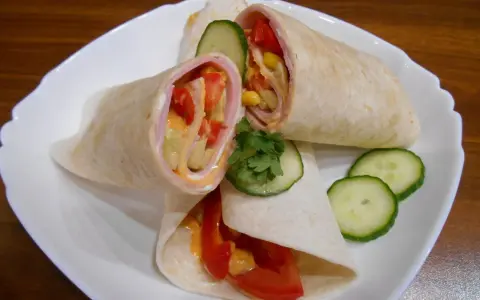 Pyszna tortilla z szynką, pomidorem, kukurydzą i ogórkiem, polana sosem. Idealna na szybki posiłek.