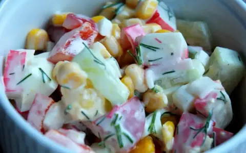 Pyszna sałatka z surimi, kukurydzą, ogórkiem i jajkiem, polana kremowym sosem.
