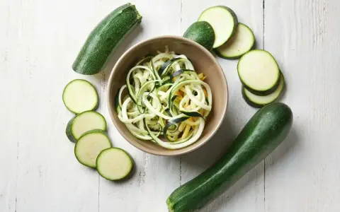 Spiralizowana cukinia w misce, otoczona świeżymi cukiniami i plasterkami. Odpowiedź na pytanie: czy można jeść surową cukinię? Tak!