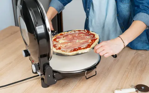 Osoba wkłada pizzę do pieca. Zastanawiasz się, w ilu stopniach piec pizzę? Ten piec jest idealny do domowych wypieków.