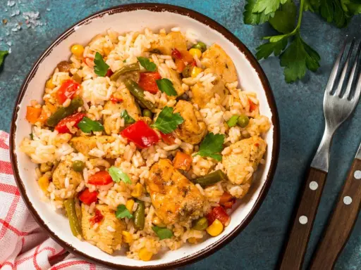 Pyszne risotto z kurczakiem i warzywami, podane w misce, obok widelca i noża.