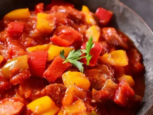 Pyszne leczo z pieczarkami, papryką i kiełbasą w sosie pomidorowym, udekorowane natką pietruszki.