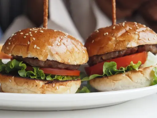 Dwa apetyczne mini burgery z sezamem, sałatą i pomidorem. Idealne na imprezę, oto prosty mini burgery przepis.
