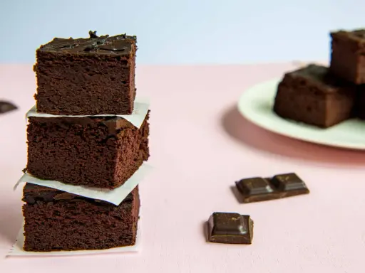 Ciemne, wilgotne brownie z fasoli ułożone w wieżę, obok kawałki czekolady.