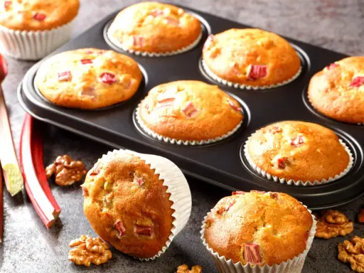 Pyszne muffinki z rabarbarem, świeże i pachnące, gotowe do podania. Obok leżą łodygi rabarbaru i orzechy włoskie.