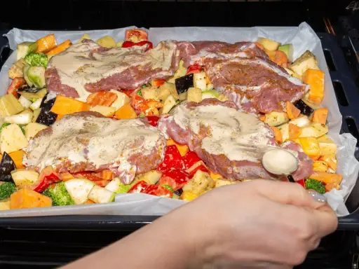 Pyszne mięso na imprezę z warzywami: ziemniaki, bataty, cukinia, brokuły, papryka i bakłażan, wszystko polane sosem.