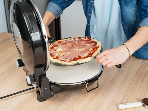 Osoba wkłada pizzę do pieca. Zastanawiasz się, w ilu stopniach piec pizzę? Ten piec jest idealny do domowych wypieków.