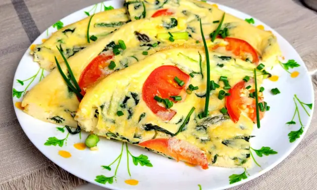 Pyszny omlet ze szpinakiem, pomidorami i szczypiorkiem, pokrojony w trójkąty, podany na talerzu z kwiatowym wzorem.