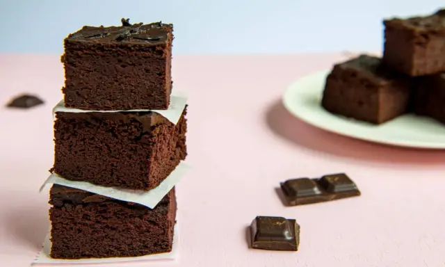 Ciemne, wilgotne brownie z fasoli ułożone w wieżę, obok kawałki czekolady.