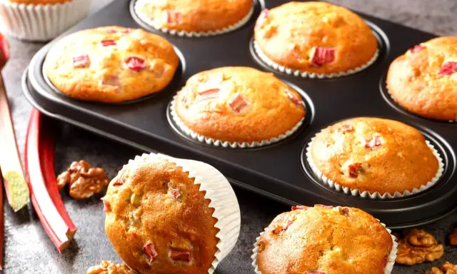 Pyszne muffinki z rabarbarem, świeże i pachnące, gotowe do podania. Obok leżą łodygi rabarbaru i orzechy włoskie.