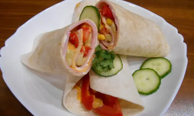 Pyszna tortilla z szynką, pomidorem, kukurydzą i ogórkiem, polana sosem. Idealna na szybki posiłek.
