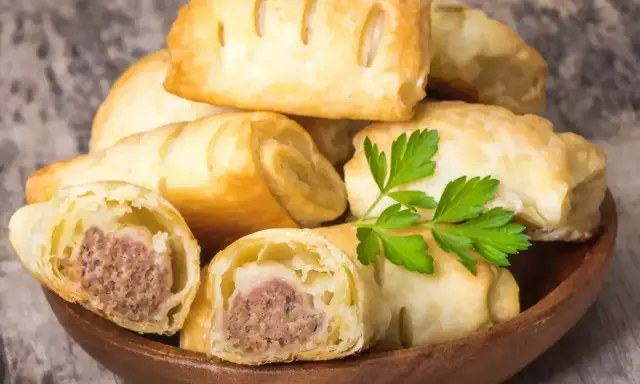 Stos pieczonego ciasta francuskiego z kiełbaską w środku, ozdobione natką pietruszki.