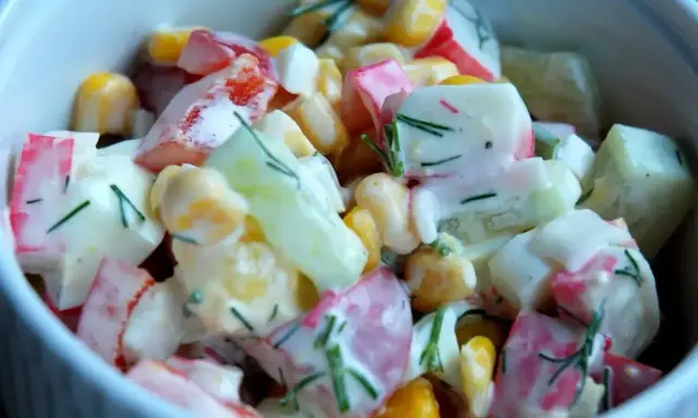 Pyszna sałatka z surimi, kukurydzą, ogórkiem i jajkiem, polana kremowym sosem.
