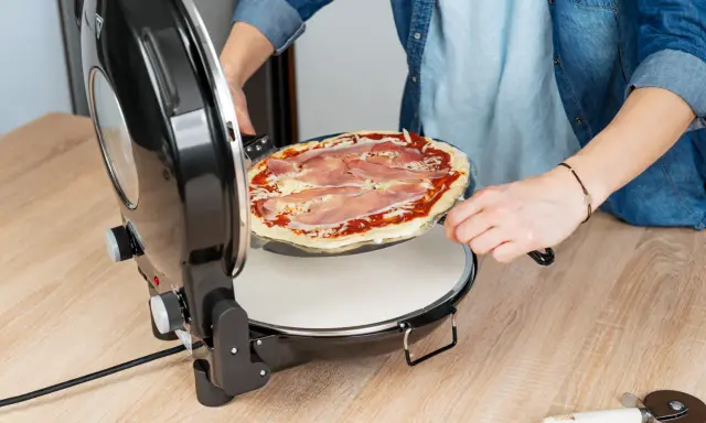 Osoba wkłada pizzę do pieca. Zastanawiasz się, w ilu stopniach piec pizzę? Ten piec jest idealny do domowych wypieków.