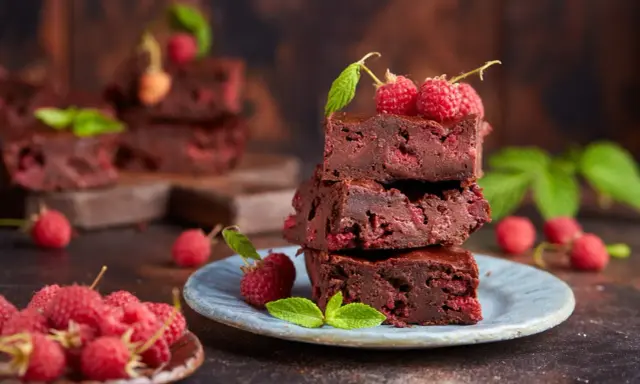 Stos puszystych brownie z malinami, ozdobiony świeżymi malinami i listkami mięty.
