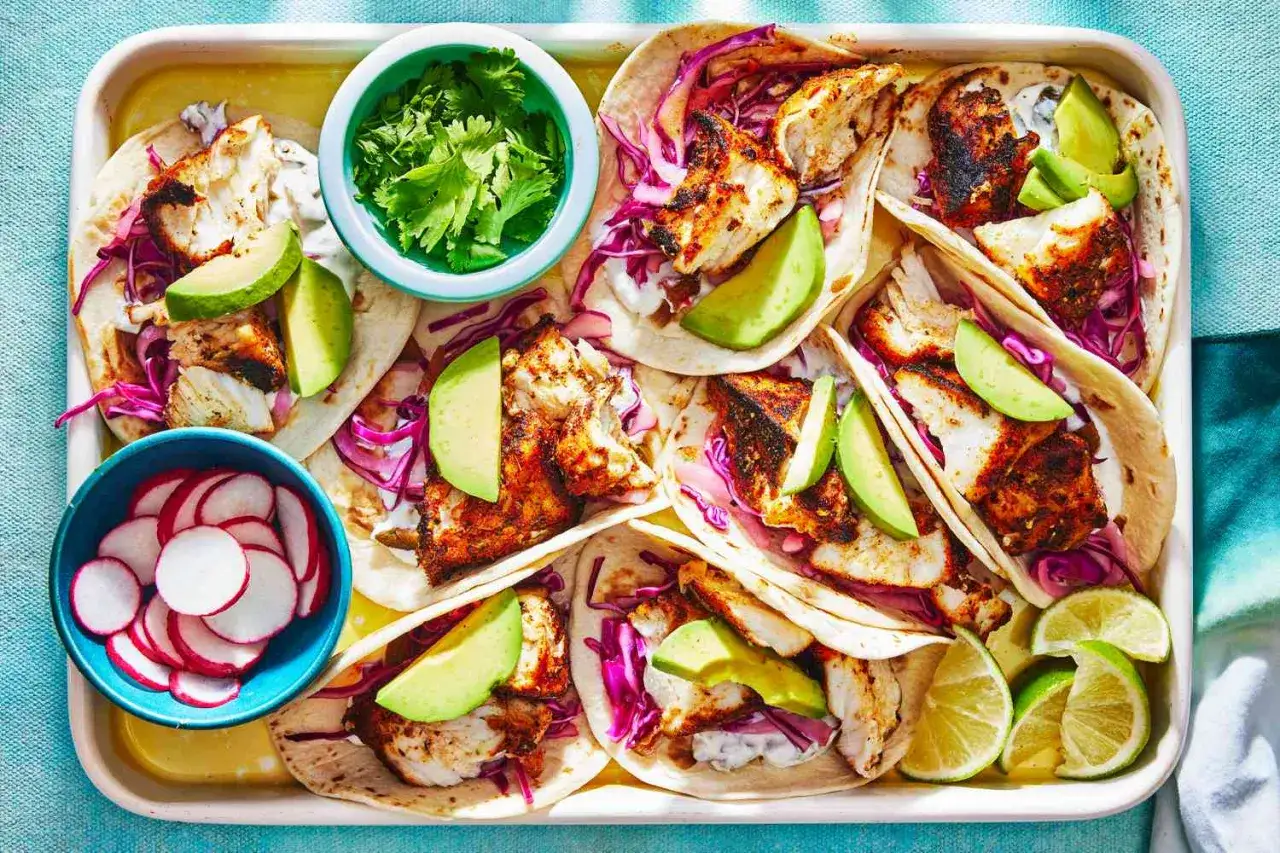 Pyszny przepis na kolację: tacos z rybą, awokado, czerwoną kapustą i kolendrą. Obok miseczki z rzodkiewką i limonką.
